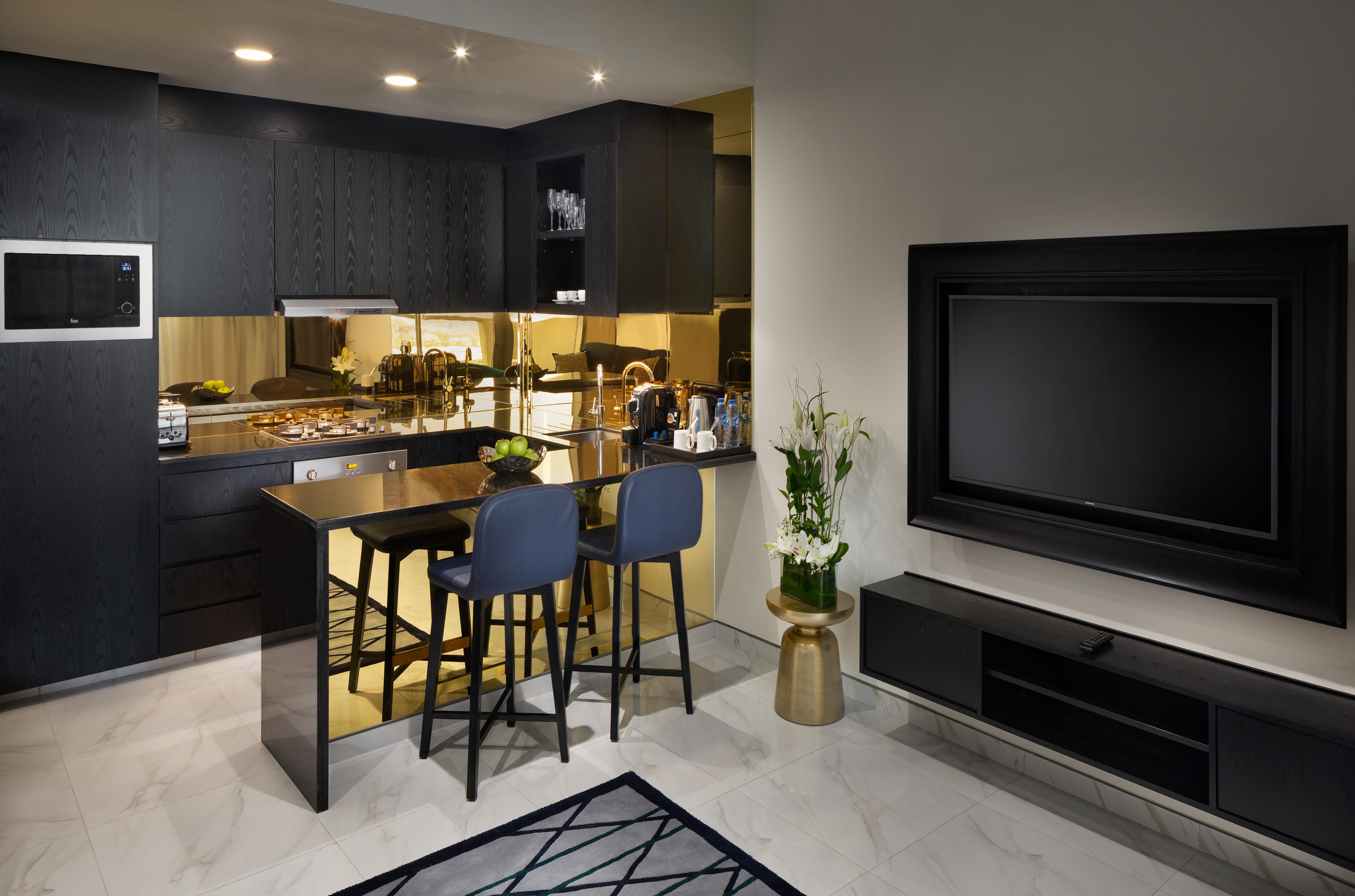 الشقق الفندقية دبيفي  ميلينيوم أتريا بيزنس باي المظهر الخارجي الصورة The photo depicts a modern kitchen and living area. The kitchen features dark cabinetry with a clean design, showcasing various appliances, including a stovetop and possibly an oven. There is a kitchen island with two stools, suggesting a space for c