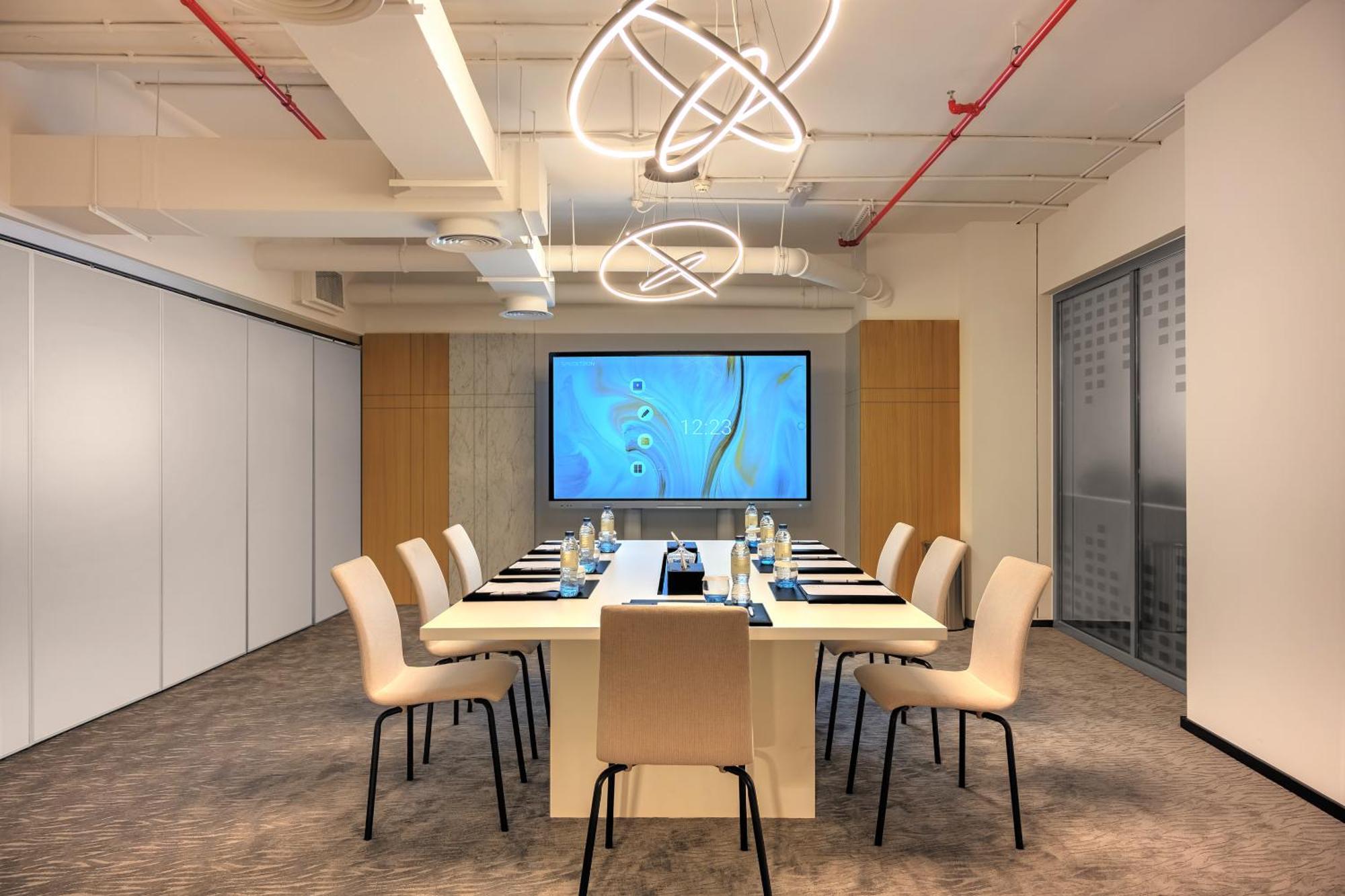 الشقق الفندقية دبيفي  ميلينيوم أتريا بيزنس باي المظهر الخارجي الصورة The photo shows a modern conference room designed for meetings. It features a long white table surrounded by beige chairs. At the end of the table, there is a large screen displaying a blue abstract design. The room is well-lit with contemporary ligh