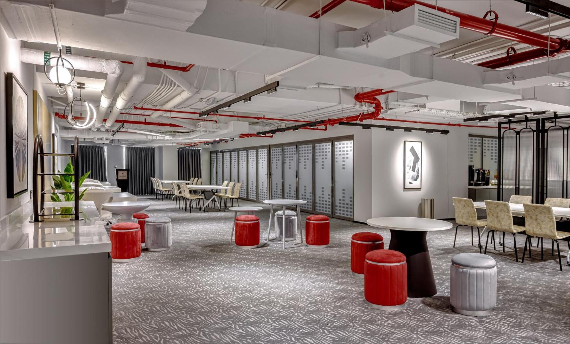 الشقق الفندقية دبيفي  ميلينيوم أتريا بيزنس باي المظهر الخارجي الصورة The photo shows a modern interior space, likely an office or communal area. The flooring is covered with a textured carpet, and the ceiling features exposed pipes painted red. 

There are several seating options, including small round tables with sto