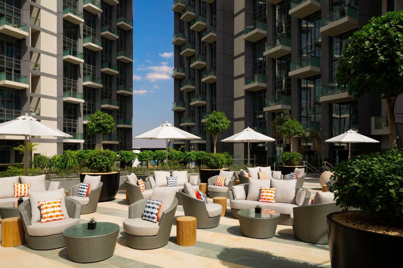 الشقق الفندقية دبيفي  ميلينيوم أتريا بيزنس باي المظهر الخارجي الصورة The photo shows a modern outdoor lounge area, featuring several comfortable seating arrangements made of soft, stylish lounge chairs and round tables. The seating is adorned with colorful pillows, adding a pop of color to the neutral tones of the fur