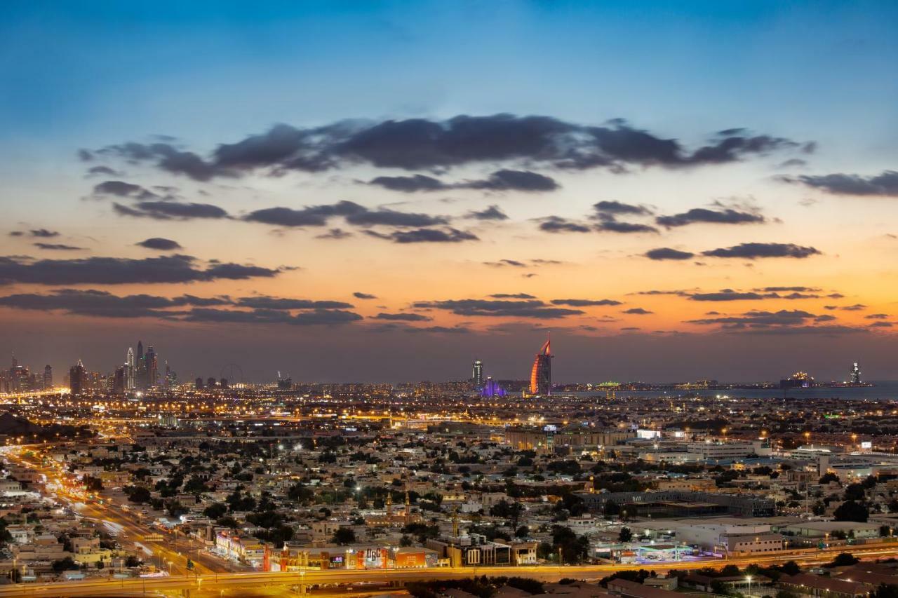 الشقق الفندقية دبيفي  ميلينيوم أتريا بيزنس باي المظهر الخارجي الصورة The photo shows a stunning cityscape at dusk, with a panoramic view of a city skyline. The sky is transitioning from blue to orange, indicating sunset, with scattered clouds creating a colorful backdrop. In the foreground, you can see a sprawling urb