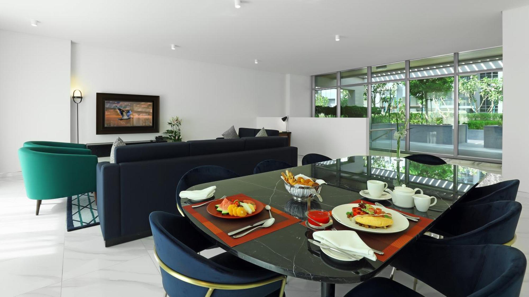 الشقق الفندقية دبيفي  ميلينيوم أتريا بيزنس باي المظهر الخارجي الصورة The photo depicts a modern living space with a dining area and a seating area. In the foreground, there is a round dining table set with plates of food, including eggs, toast, and a small bowl of fruit, accompanied by cups and napkins. The table is c